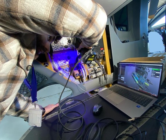 Ingenieur erfasst die Innenstruktur eines Flugzeugcockpits mit einem handgeführten 3D‑Scanner, während Echtzeit‑Scandaten in der 3D‑Messsoftware auf einem Laptop angezeigt werden. 